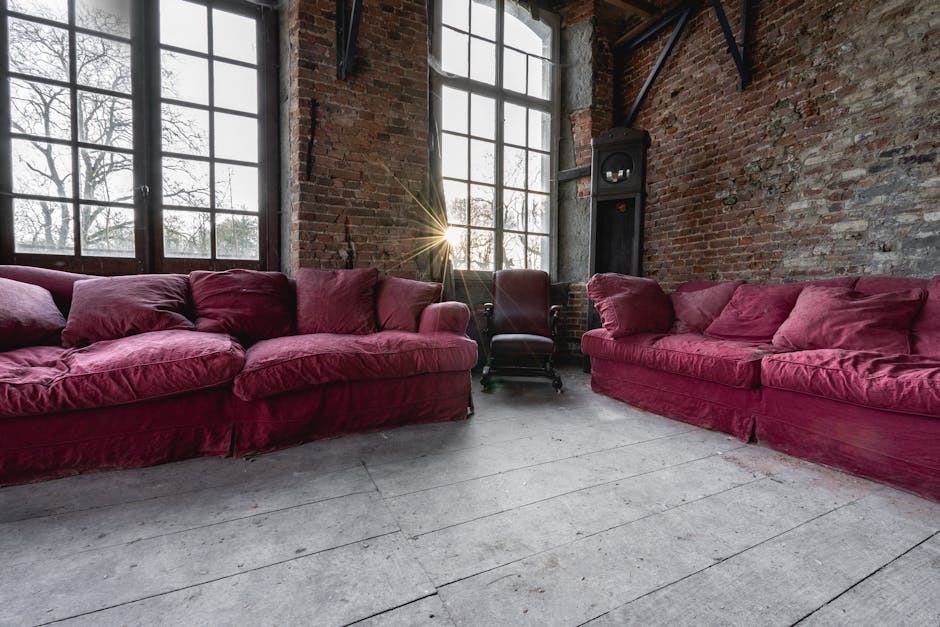 A photograph shows two vintage-style upholstered armchairs positioned on a concrete floor against a plain, light-colored wall. The left armchair features a tall, white-painted wooden frame with a high